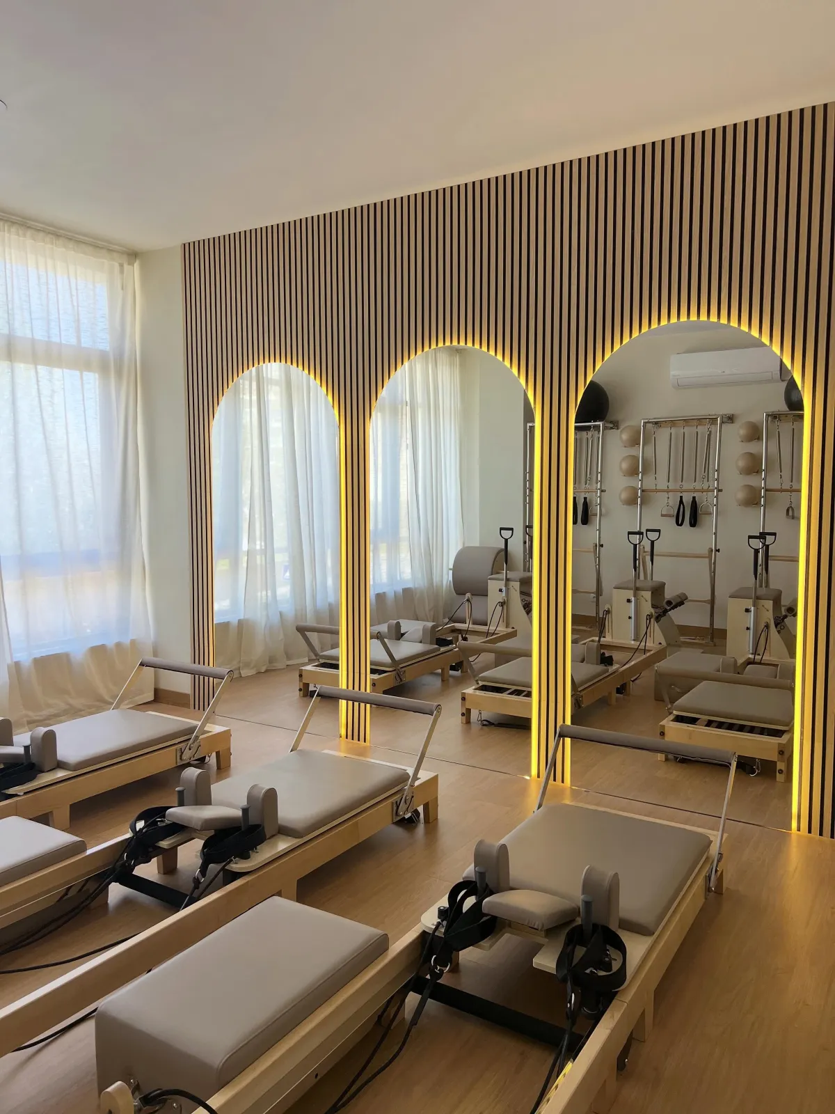 Estúdio de pilates da Clínica ReForm, com reformers, ripas de madeira e espelhos em arco iluminados